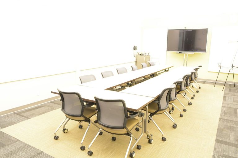 A view of a smart room l in a table group configuration with a tv and whiteboards